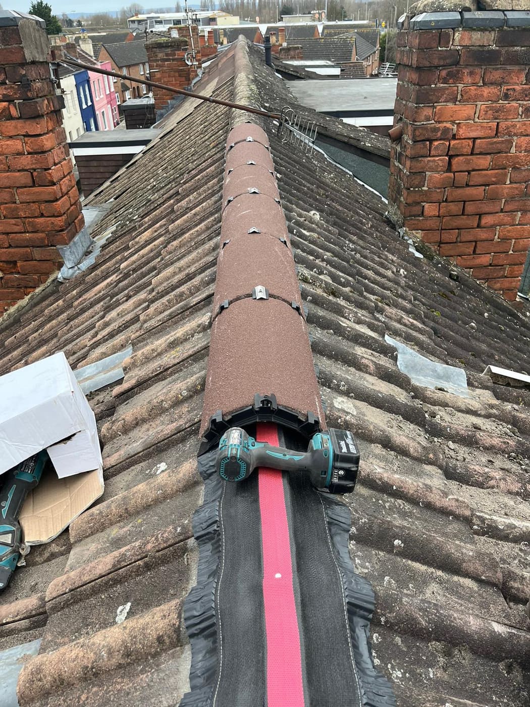 Ridge tiles being mechanically fixed over ventilated dry ridge roll, cordless drill in place